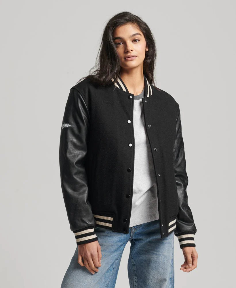 Person wearing a black varsity jacket with leather sleeves on a gray background